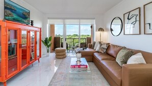 A living room with a brown sofa, a glass coffee table with a book, a red cabinet, and a large TV screen. - Coconut Grove Retreat, Bayviews, 1 Park Incl, Wkspace, Smart TV, Pool/hottub" (Miami)