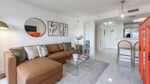 A modern living room with a brown sofa, a glass coffee table, and a kitchen area in the background. - Coconut Grove Retreat, Bayviews, 1 Park Incl, Wkspace, Smart TV, Pool/hottub" (Miami)