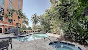 A swimming pool area with lounge chairs and a covered seating area, surrounded by palm trees and a building. - Coconut Grove Retreat, Bayviews, 1 Park Incl, Wkspace, Smart TV, Pool/hottub" (Miami)