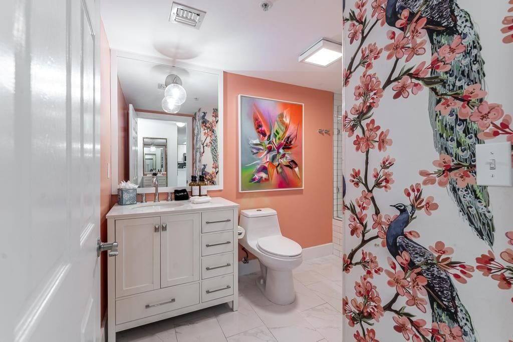 Ein Badezimmer mit weißem Waschtisch, Toilette und Wandgestaltung mit Pfauhen- und Blumendesign.