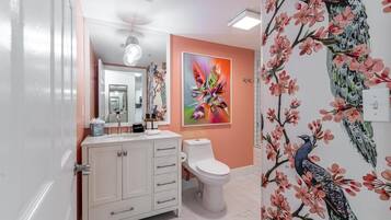 Ein Badezimmer mit weißem Waschtisch, Toilette und Wandgestaltung mit Pfauhen- und Blumendesign.