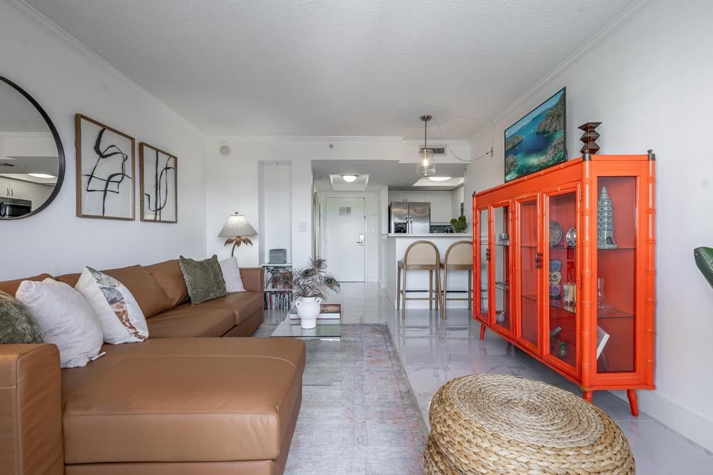 A modern living room with a brown sofa, a woven ottoman, and a red cabinet with glass doors.