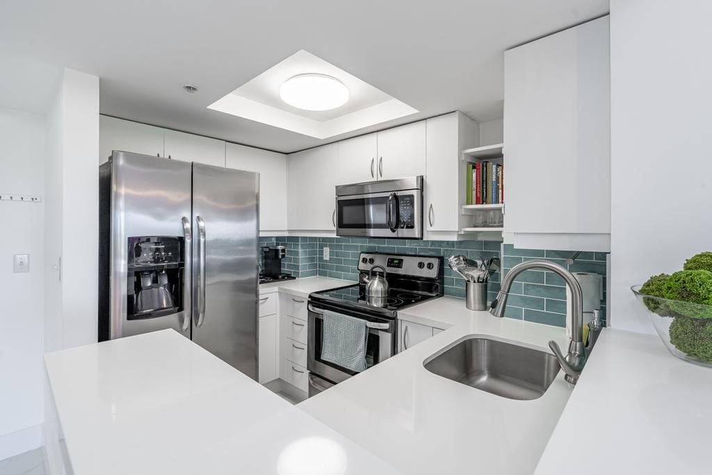A modern kitchen with stainless steel appliances, a white countertop, and a skylight.