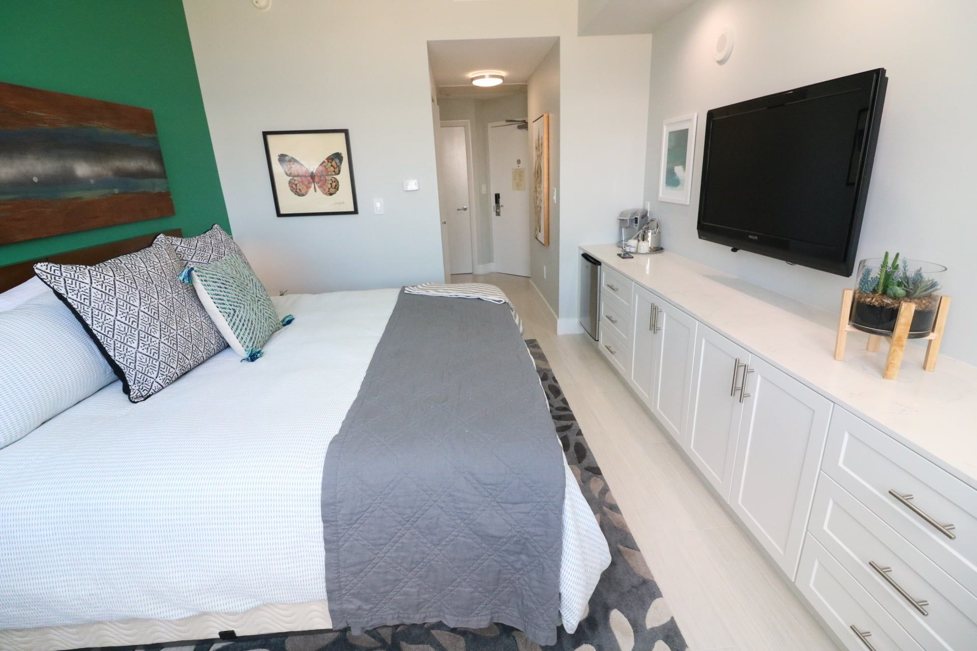 Un dormitorio con cama, almohadas, una mesita de noche, un televisor de pantalla plana y una pequeña planta en maceta.