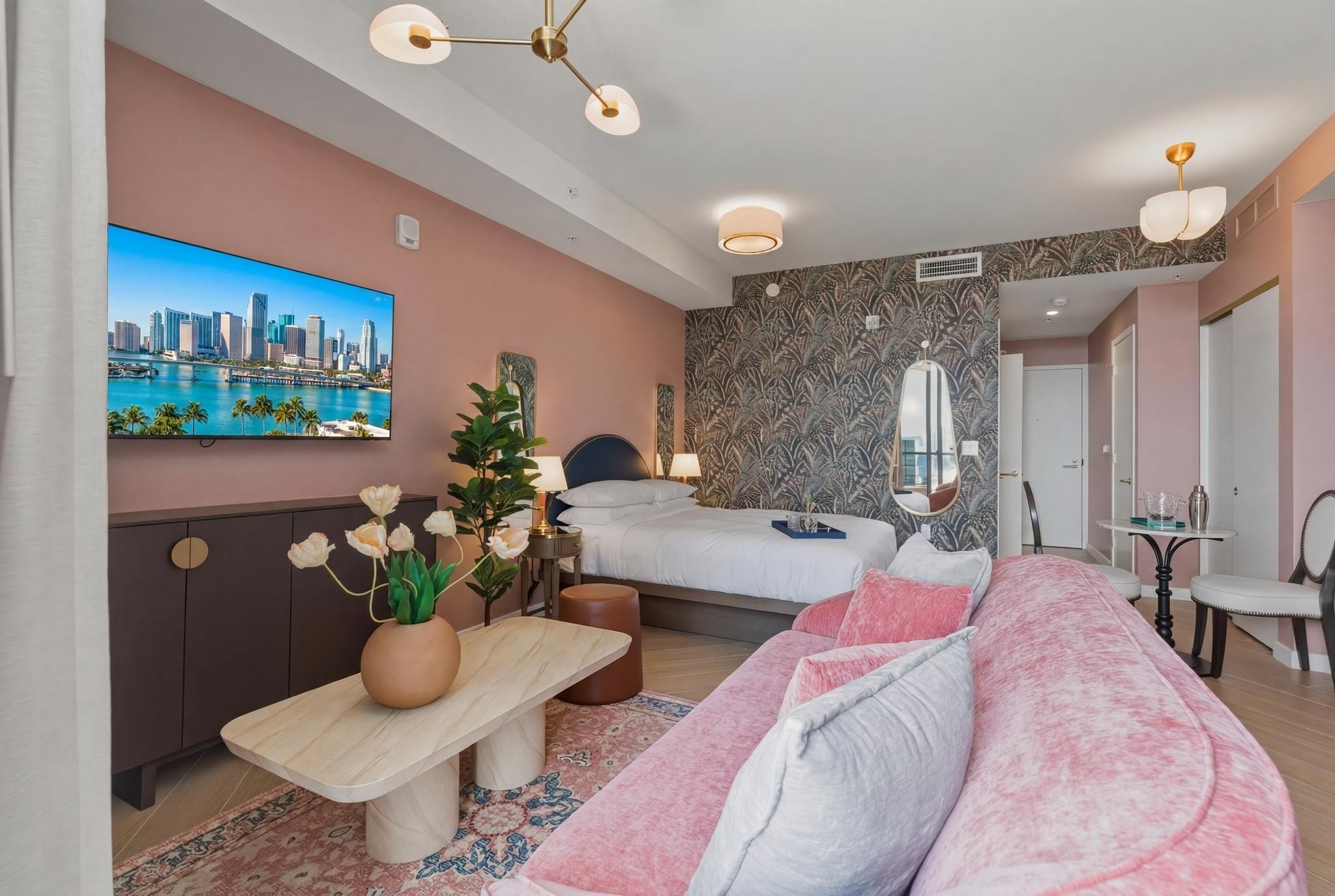 A modern hotel room with a bed, a sofa, a TV, and a desk with a plant.