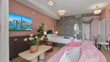 A modern hotel room with a bed, a sofa, a TV, and a desk with a plant.