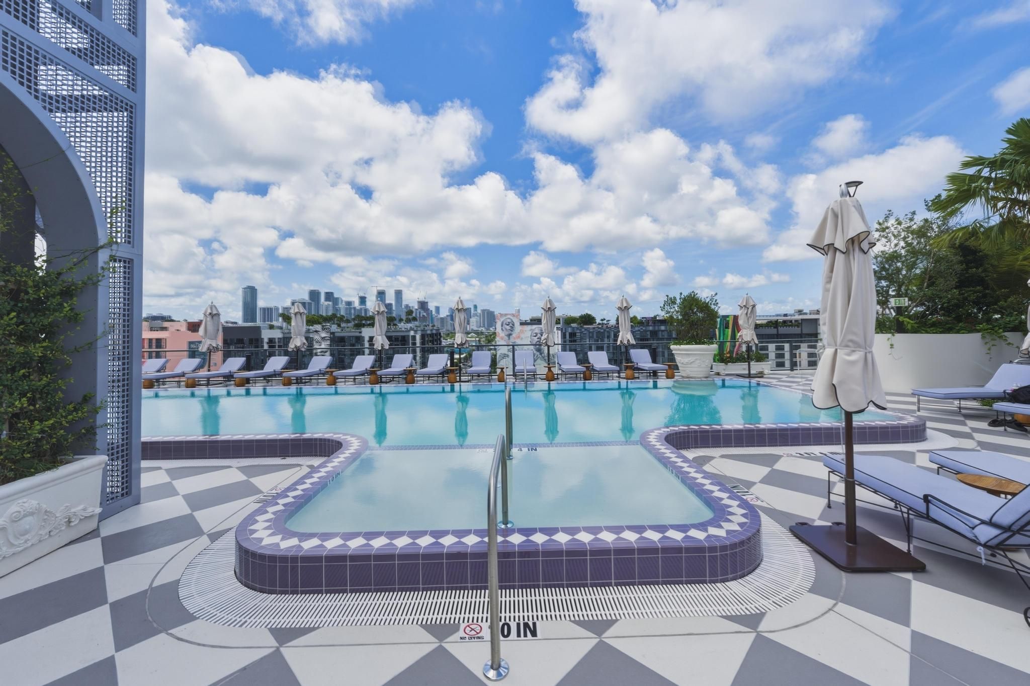 A rooftop pool with lounge chairs and a city skyline in the background.