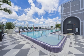 A pool area with lounge chairs, a hot tub, and a building with an exit sign. - Designer Studio With Balcony Walk to Restaurants, Art & Nightlife (Miami)