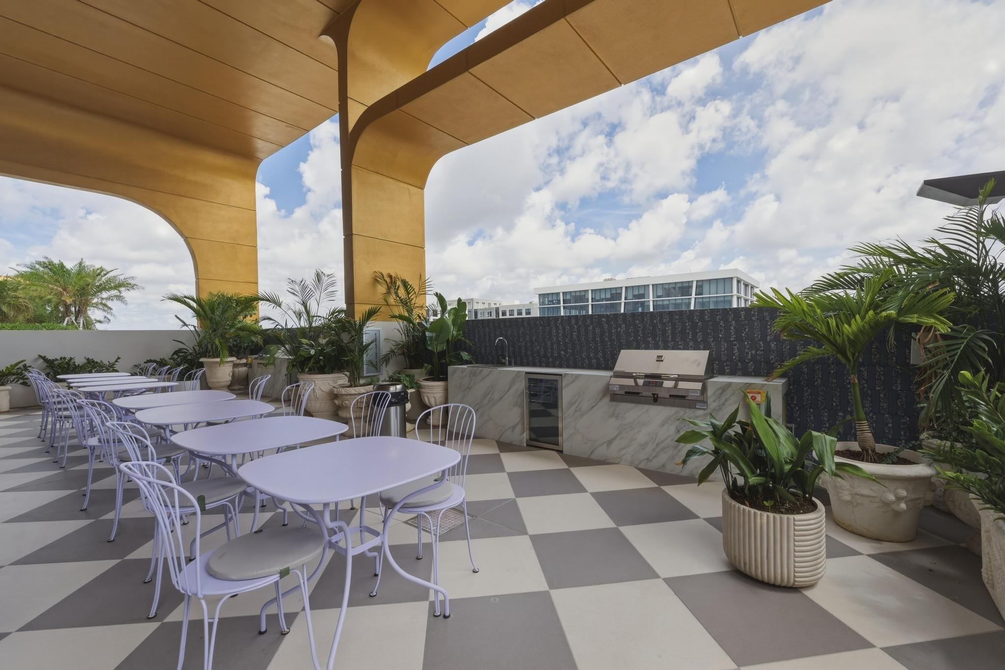 Een terras buiten met tafels, stoelen, een barbecue en potplanten.