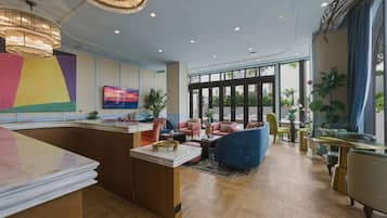 Een moderne hotellobby met een receptiebalie, een zithoek, grote ramen en decoratieve planten.