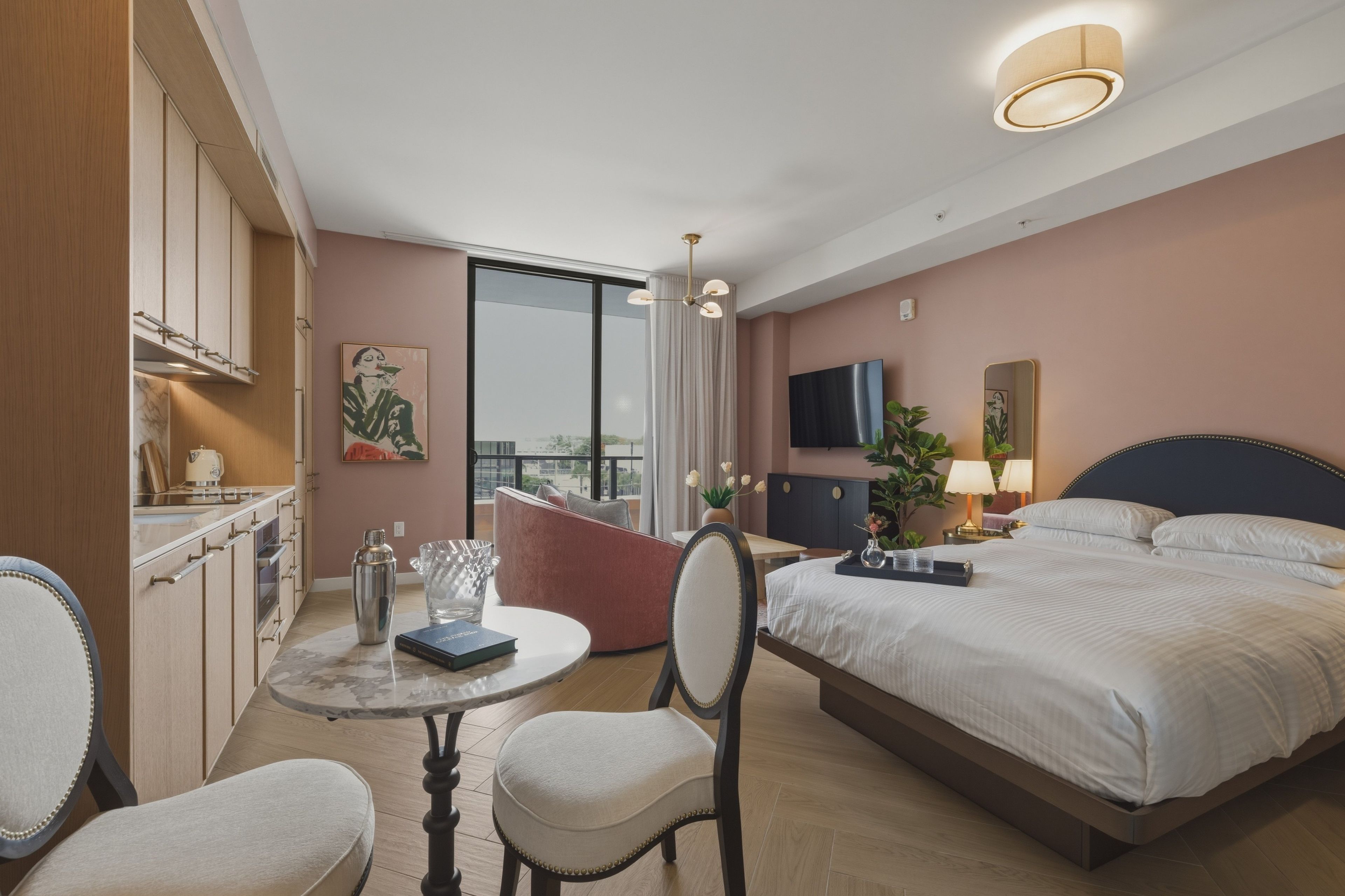 A hotel room with a bed, a dining table, a chair, a TV, and a large window.