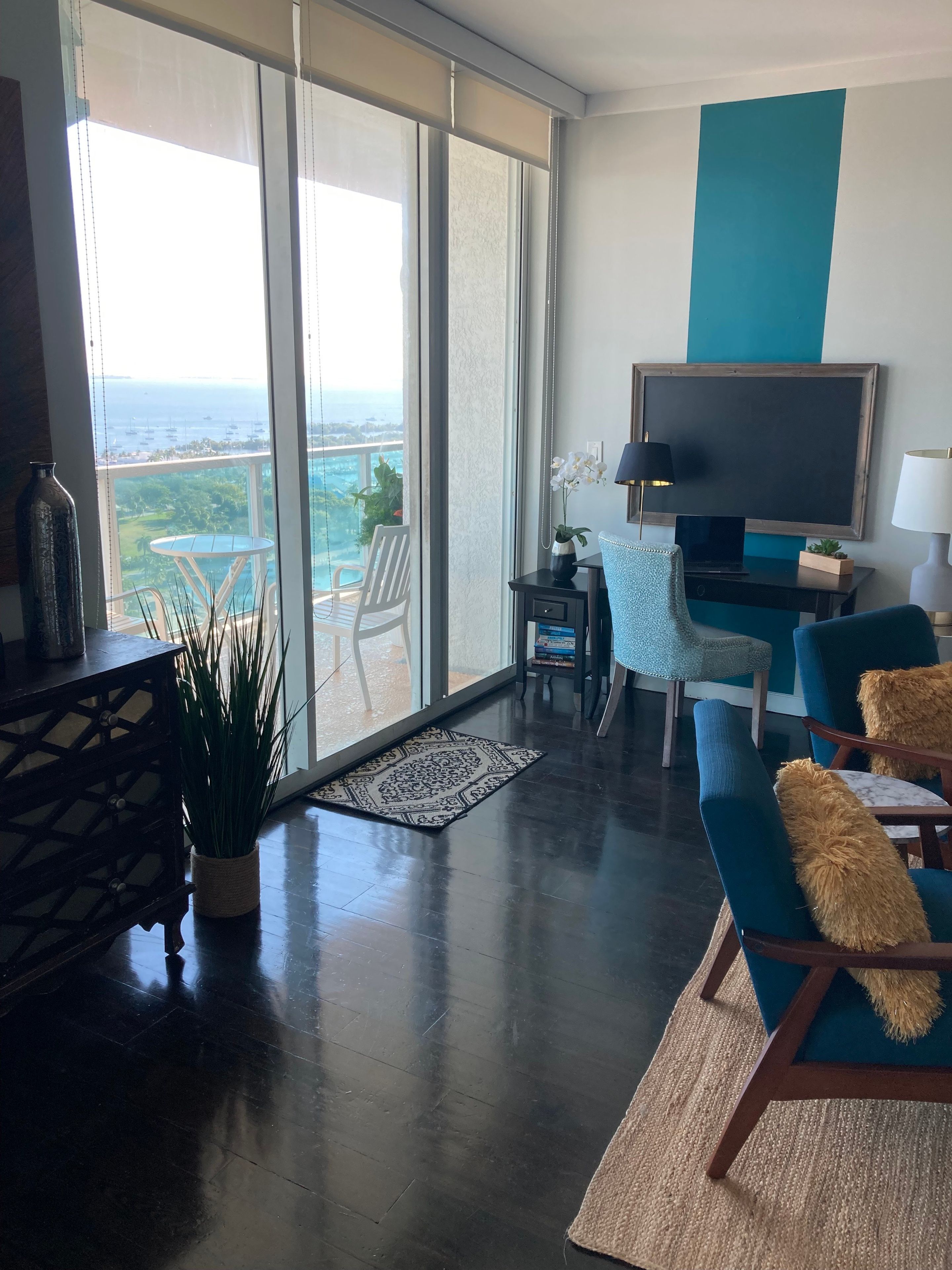 Een moderne woonkamer met een grote schuifpui naar een balkon, een flatscreen televisie, een kleine tafel met een lamp en comfortabele zitplaatsen.
