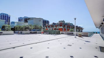 A rooftop terrace with a view of the sea, featuring a seating area with benches and potted plants.
