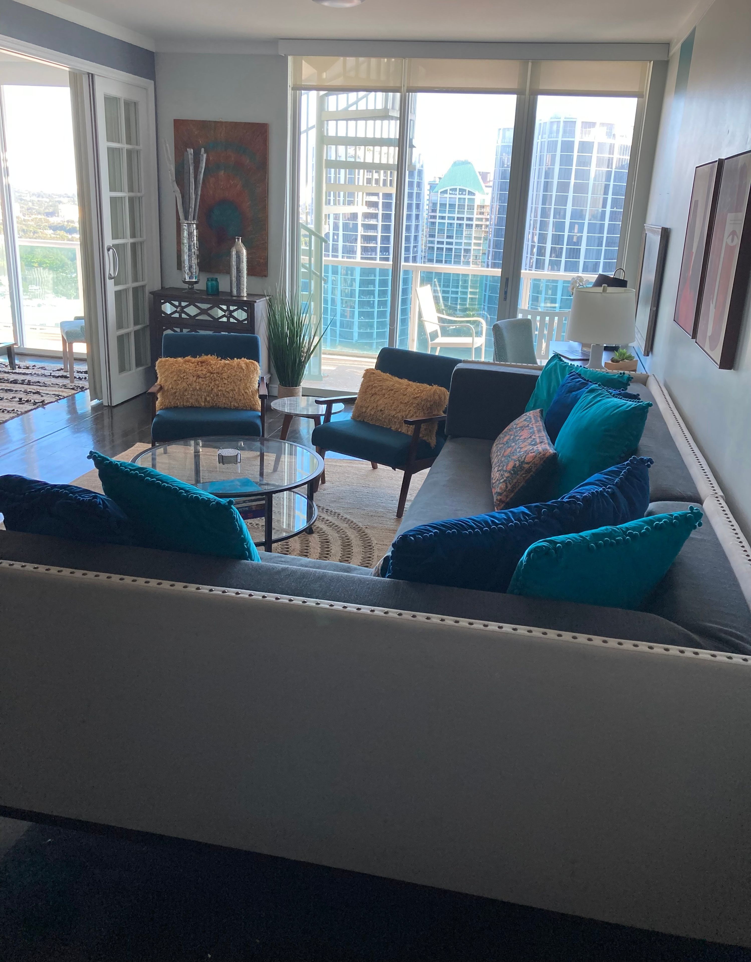 Ein modernes Wohnzimmer mit einer Couch, Sesseln, einem Couchtisch und Blick auf die Stadt durch große Fenster.