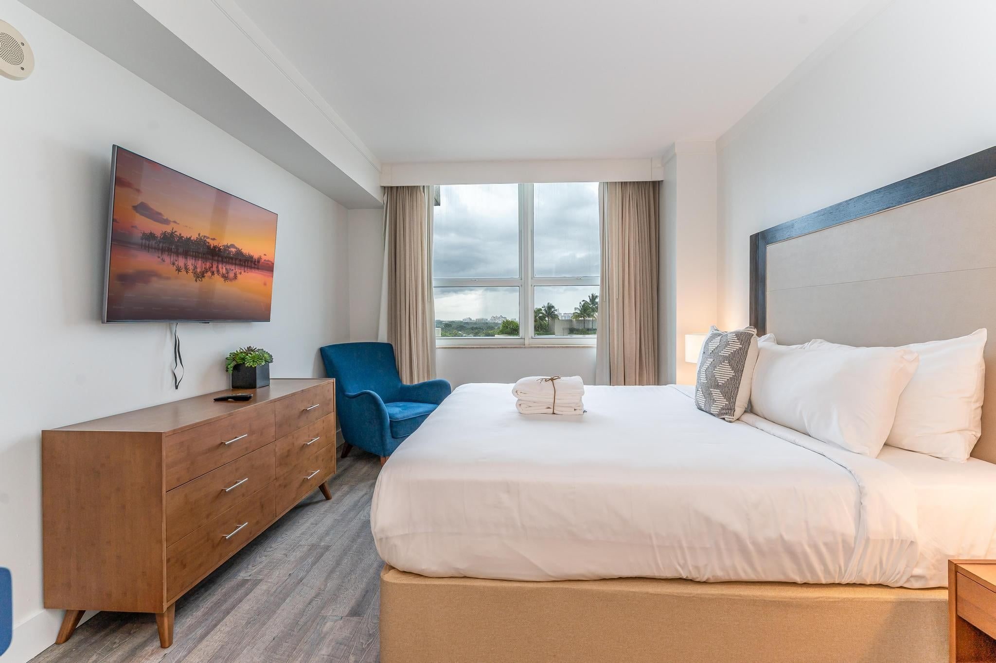A hotel room with a bed, a dresser, a chair, a TV, and a window with a view.