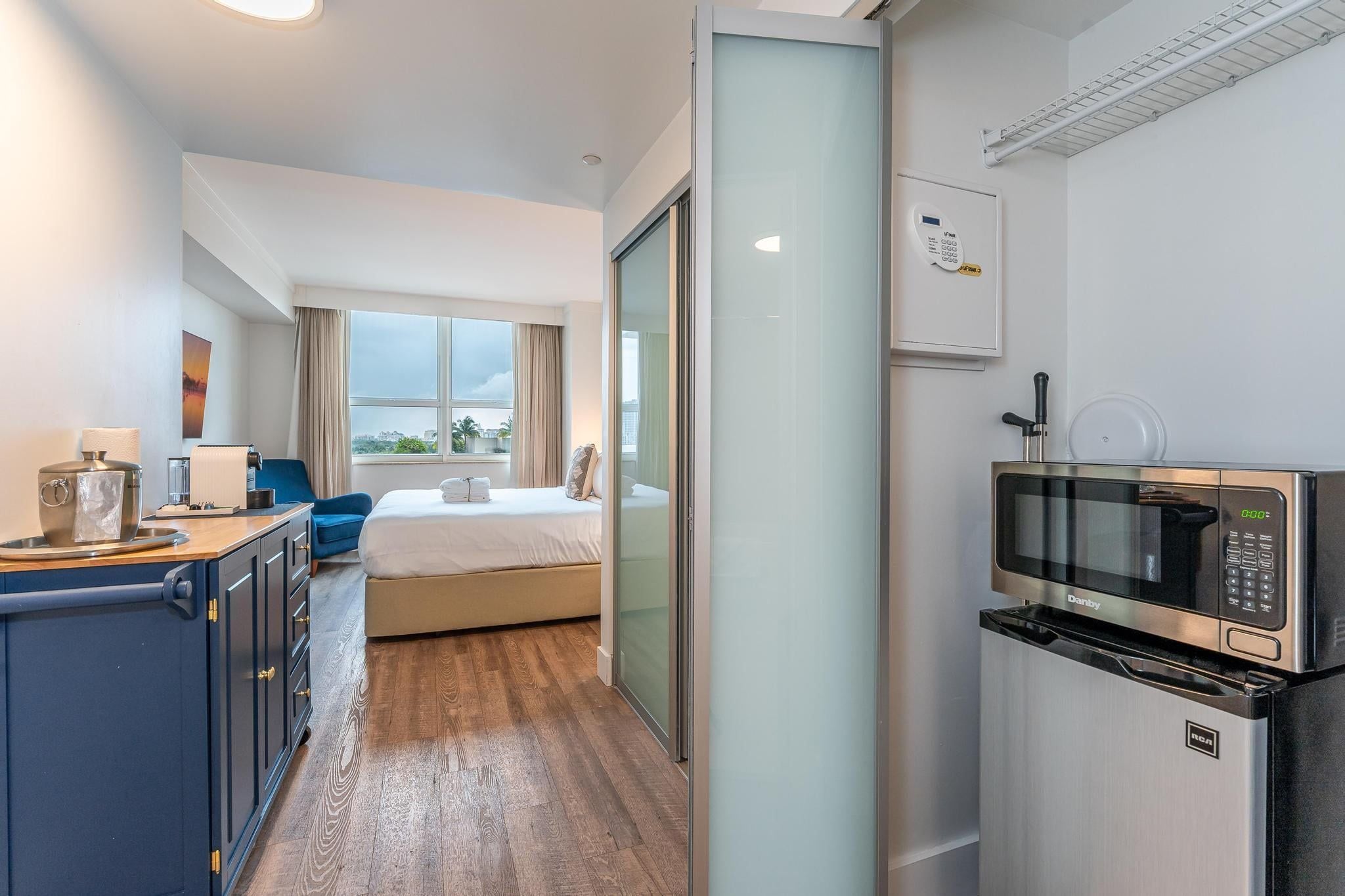 Habitación de hotel con una cama, un escritorio con computadora, un microondas y vista a la ciudad.