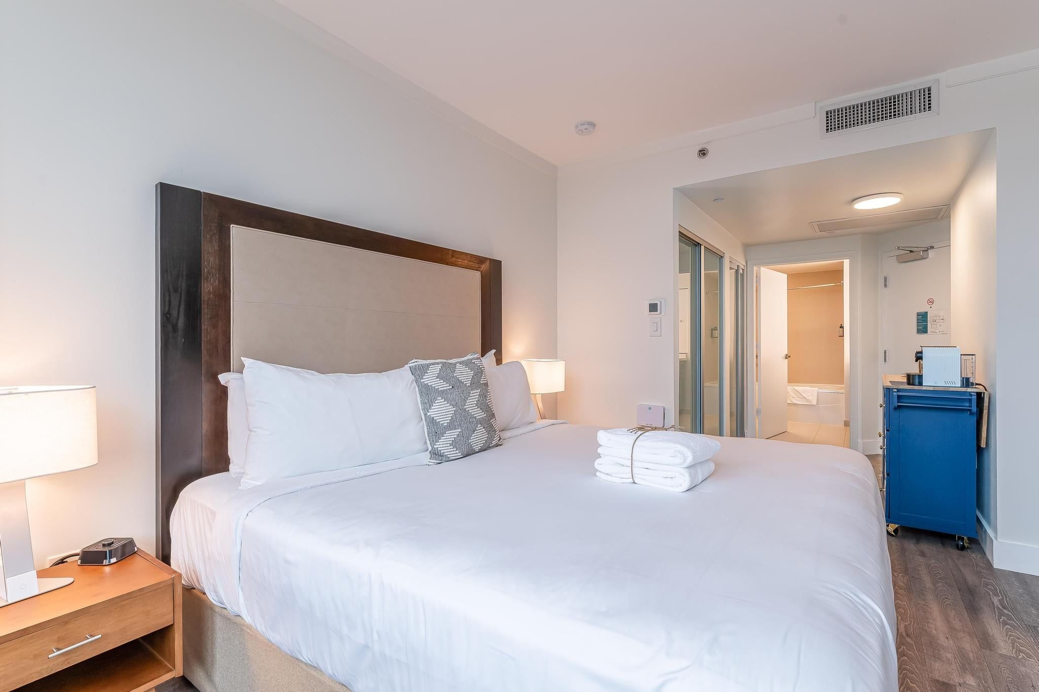 A hotel room with a large bed, a bedside table, a lamp, and a blue cabinet.