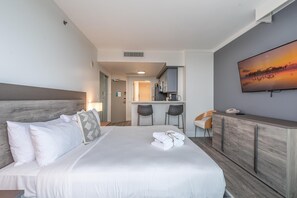 A hotel room with a bed, a desk, a chair, a TV, and a kitchen area in the background. - Connected Hotel Arya Studios 2 Beds, 2 Baths, Kitchen + Free 2-car Parking (Miami)