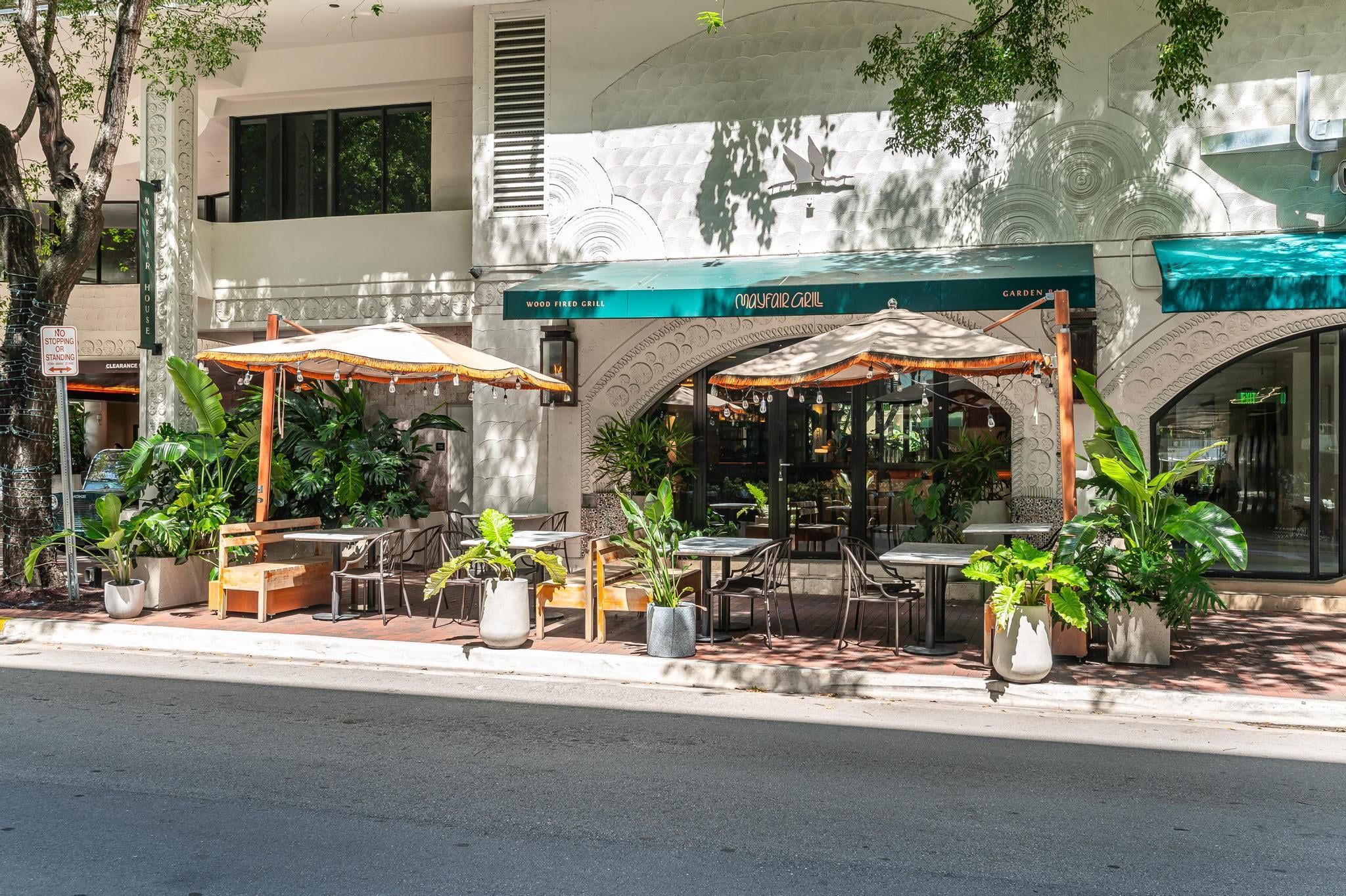 An outdoor cafe with tables and chairs, surrounded by potted plants.