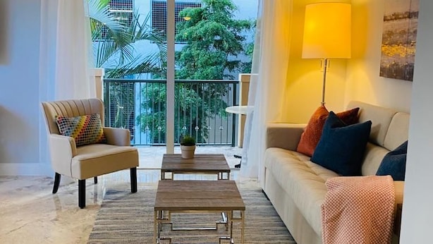 Een woonkamer met een bank, fauteuil, salontafel en een balkon met uitzicht op groen.