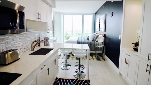 A modern kitchen with a central island, stainless steel appliances, and a large window providing a view. - Coconut Grove 21st Floor Private Studio-parking & Wifi Included (Miami)