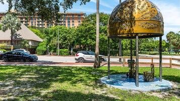Ein Pavillon mit goldenem Blattmuster, umgeben von Gras und Bäumen, mit einem Gebäude und geparkten Autos im Hintergrund.