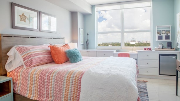 Quarto com uma cama grande, janela com vista para a cidade, mesa de cabeceira e cômoda.