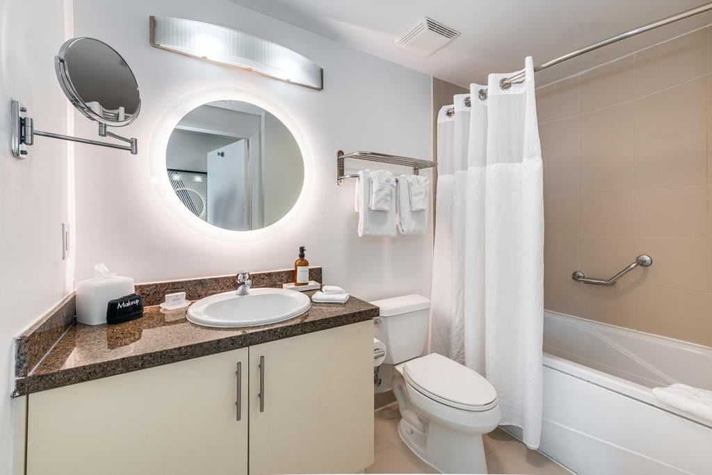 A modern bathroom with a round mirror, a sink, a toilet, and a shower area.