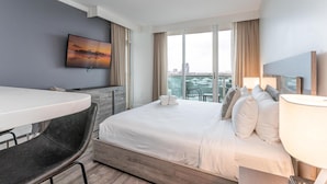 Ett hotellrum med en säng, ett skrivbord, en stol, en tv och utsikt över staden.