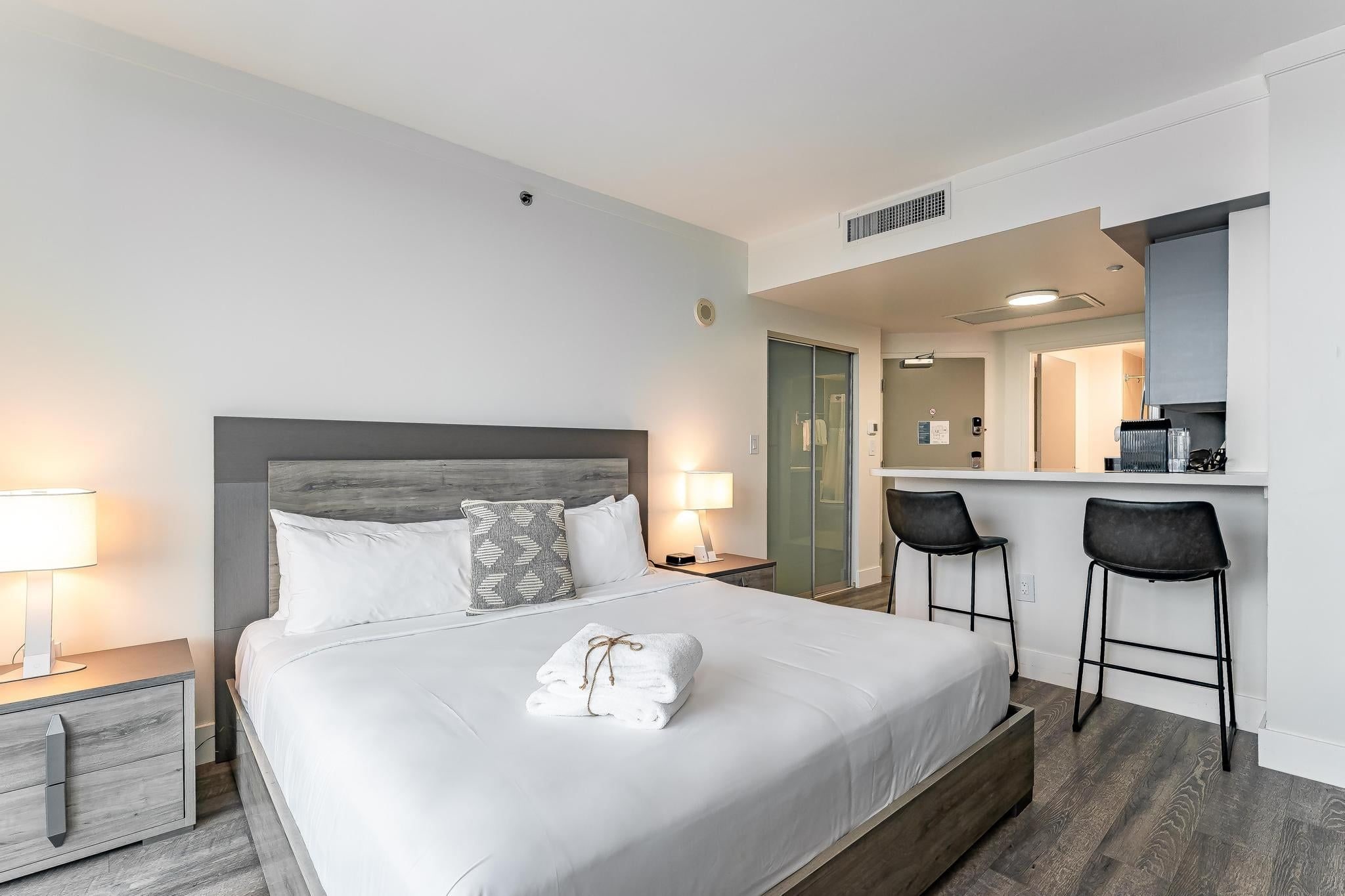Een hotelkamer met een groot bed, nachtlampjes, een bureau met stoel, en een badkamer zichtbaar door een geopende deur.