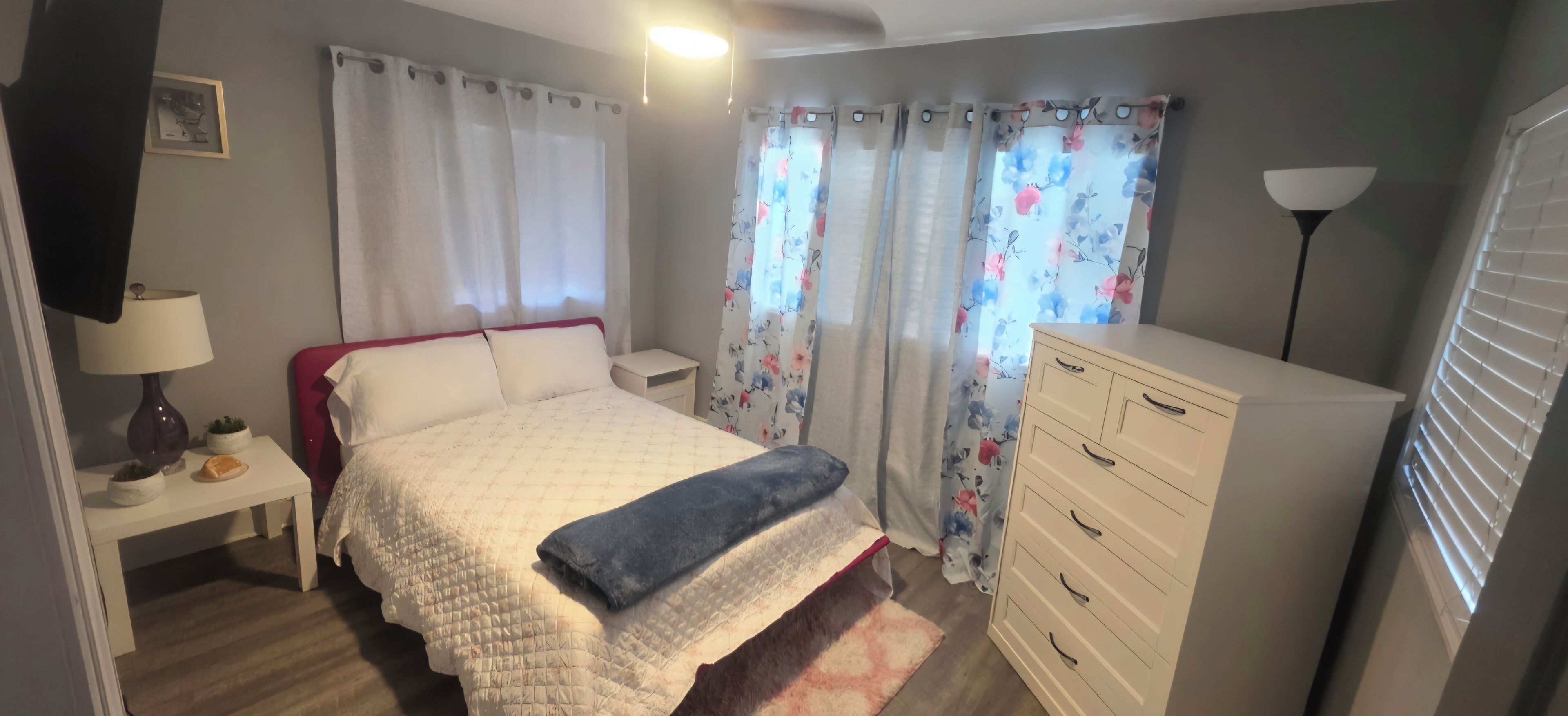 Une chambre à coucher comprenant un lit, une table de chevet, une lampe, une commode et des rideaux.