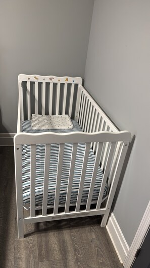 A white crib with a striped mattress and a pillow with a dotted pattern. - Tampa Home: 3-Bedroom Condo in Downtown, Near the Beach and Cruise Port (Tampa)