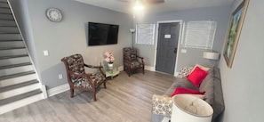 A living room with a staircase, two armchairs, a glass coffee table, a sofa, a TV, and a door with a sign. - Vrbo Property (Tampa)