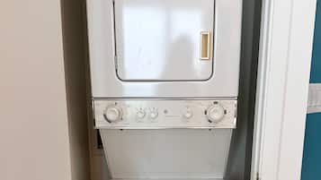 A compact, white laundry machine with a control panel, located in a small room with a tiled floor and a door on the left.