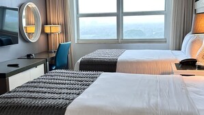 Ett hotellrum med två sängar, ett skrivbord, en TV och ett stort fönster.
