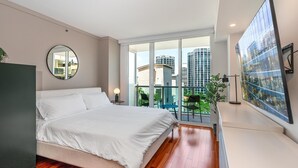 Un dormitorio moderno con una cama grande, un espejo redondo, un balcón con vistas a edificios y una obra de arte de gran formato en la pared.