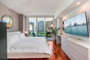 A modern bedroom with a large bed, a television on a white console, and a balcony with a city view. - Coconut Grove Studio: Sleeps 4 Includes Parking (Miami)