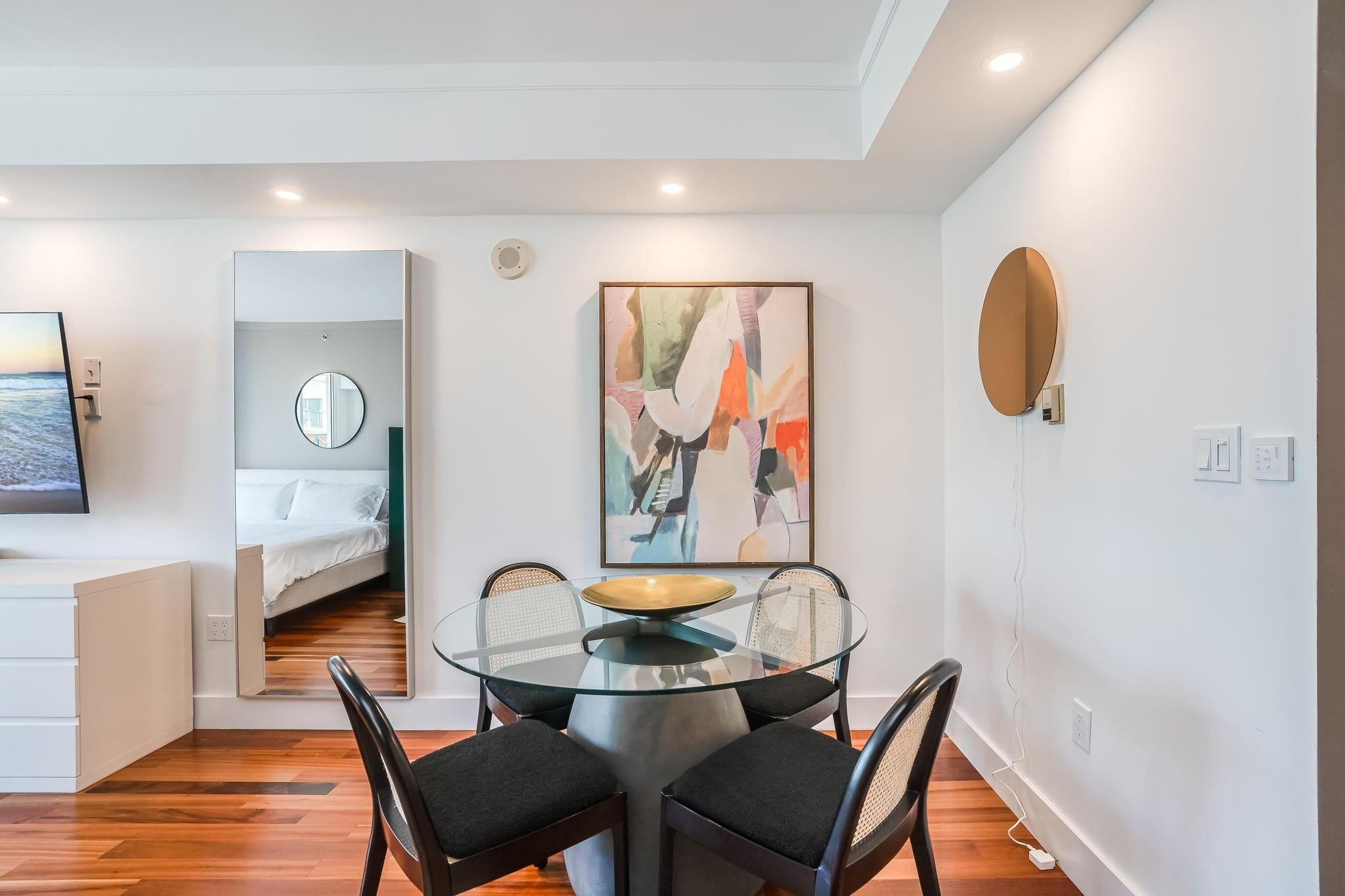 Un comedor moderno con una mesa de vidrio, sillas negras y un cuadro contemporáneo.
