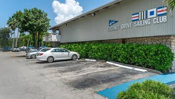 Un edificio con un letrero que indica Coconut Grove Sailing Club, espacios de estacionamiento y un cielo despejado.