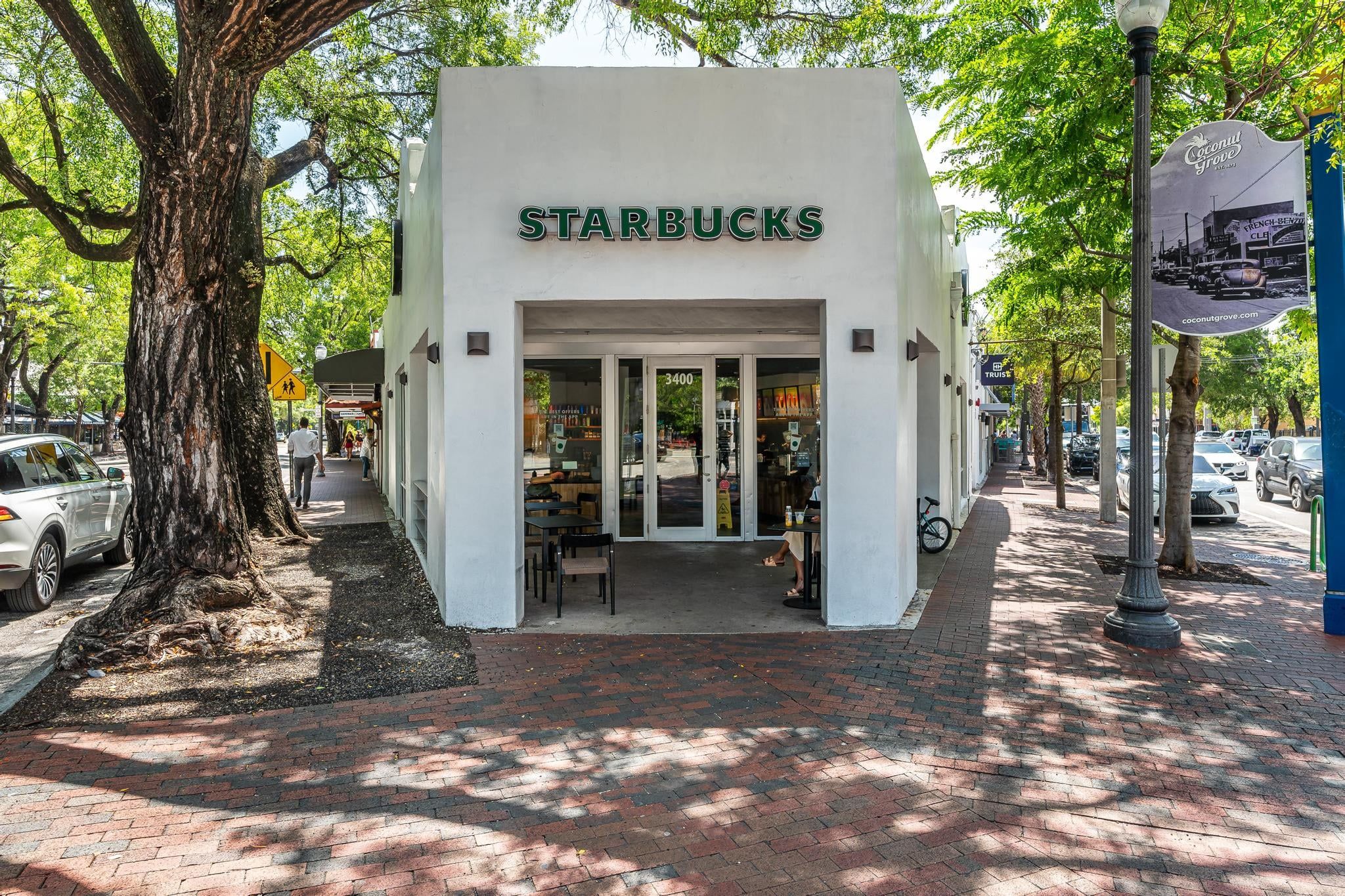 Un Starbucks à l’extérieur blanc, avec des portes en verre et une entrée pavée de briques.