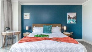 A hotel room with a large bed, two bedside tables with lamps, a desk with a chair, and a view of a swimming pool through the window. - Sunset Suite Skyline Views King + Twin Sofa Includes Parking (Miami)