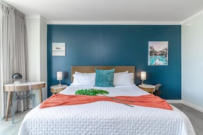 Une chambre d’hôtel avec un grand lit, deux tables de chevet avec des lampes, un bureau avec une chaise et une vue sur une piscine par la fenêtre.