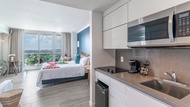 A modern hotel room with a balcony, a bed, a kitchen area with a microwave, and a coffee machine. - Sunset Suite Skyline Views King + Twin Sofa Includes Parking (Miami)