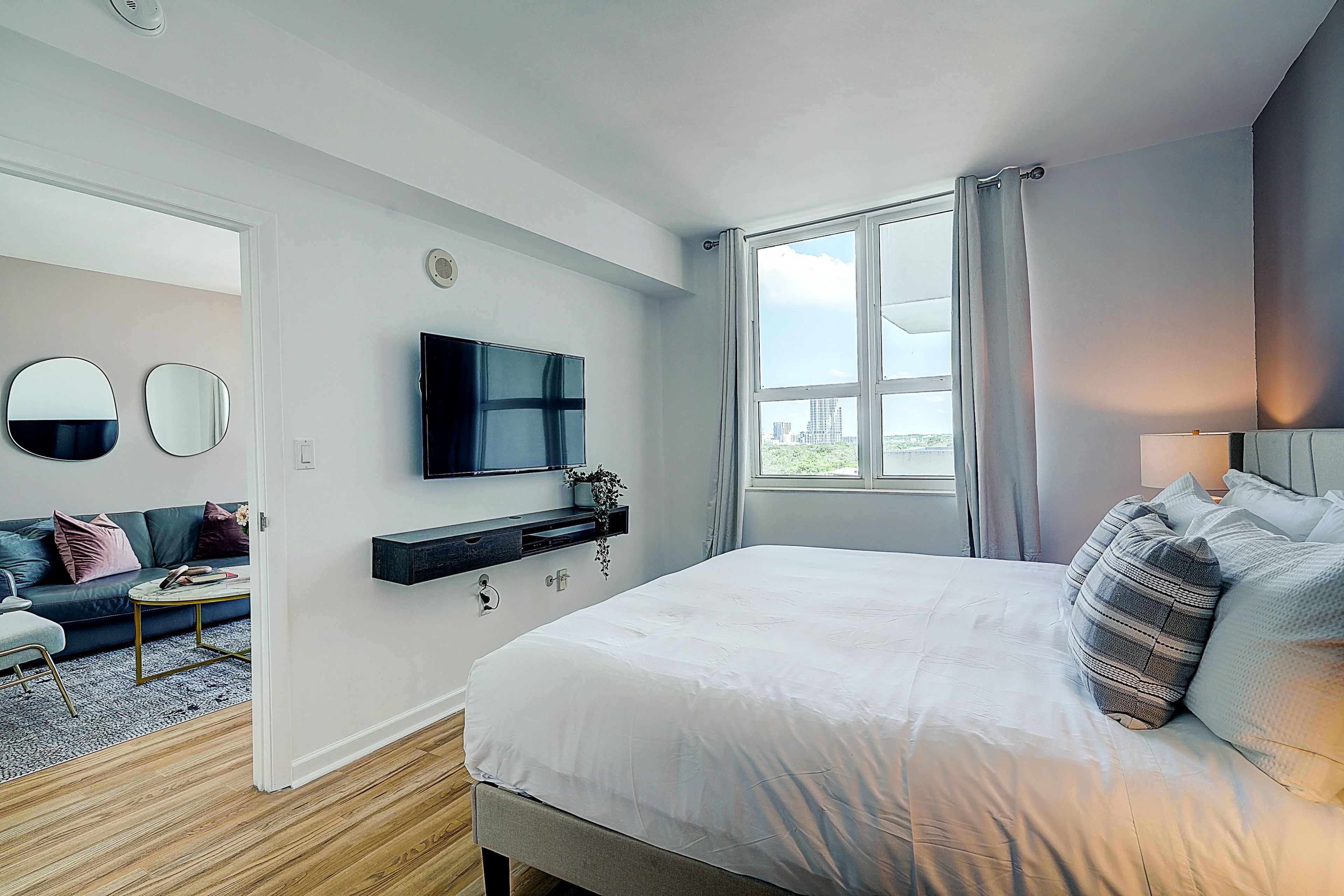 Une chambre moderne avec un grand lit, un téléviseur fixé au mur, un canapé et une fenêtre avec des rideaux.