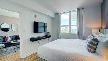 Une chambre moderne avec un grand lit, un téléviseur fixé au mur, un canapé et une fenêtre avec des rideaux.