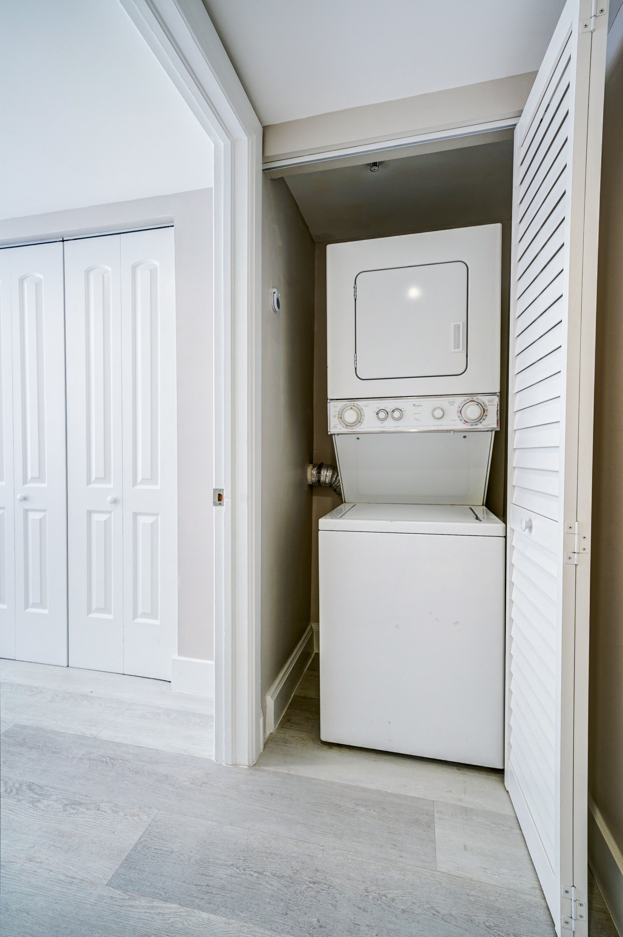 Un lavadero con lavadora y secadora apiladas, una puerta blanca y una pared color beige.