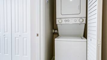 Un lavadero con lavadora y secadora apiladas, una puerta blanca y una pared color beige.