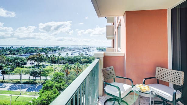 A balcony with a view of a marina and cityscape. There are two chairs and a table with a plate of food. - Coconut Grove Beauty! 1/1 Bayview Condo w/ Free Parking (Miami)