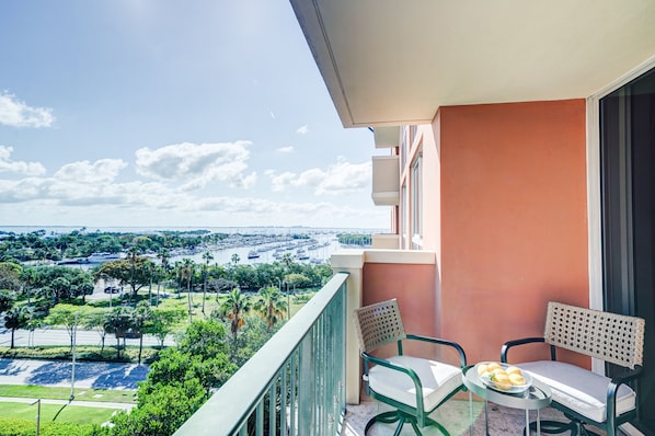 A balcony with a view of a marina and cityscape. There are two chairs and a table with a plate of food. - Coconut Grove Beauty! 1/1 Bayview Condo w/ Free Parking (Miami)