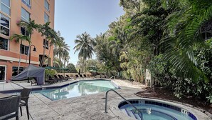 A swimming pool area with lounge chairs and a covered seating area, surrounded by palm trees and a building. - Coconut Grove Beauty! 1/1 Bayview Condo w/ Free Parking (Miami)